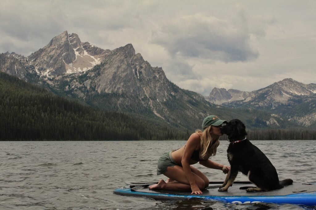 Blonde Kissing Dog on Paddleboard on Lake in Mountains