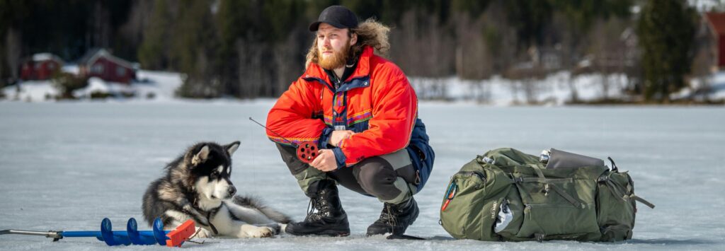 A man and his husky enjoy a winter ice fishing trip on a frozen lake.